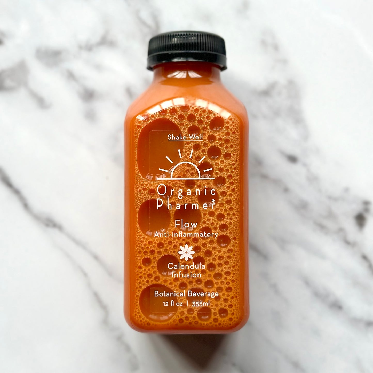 A bottle of Organic Pharmer Flow Botanical Beverage with a orange-hued liquid visible through the clear bottle. The label displays the brand name, product name, and the phrase 'Botanical Beverage.