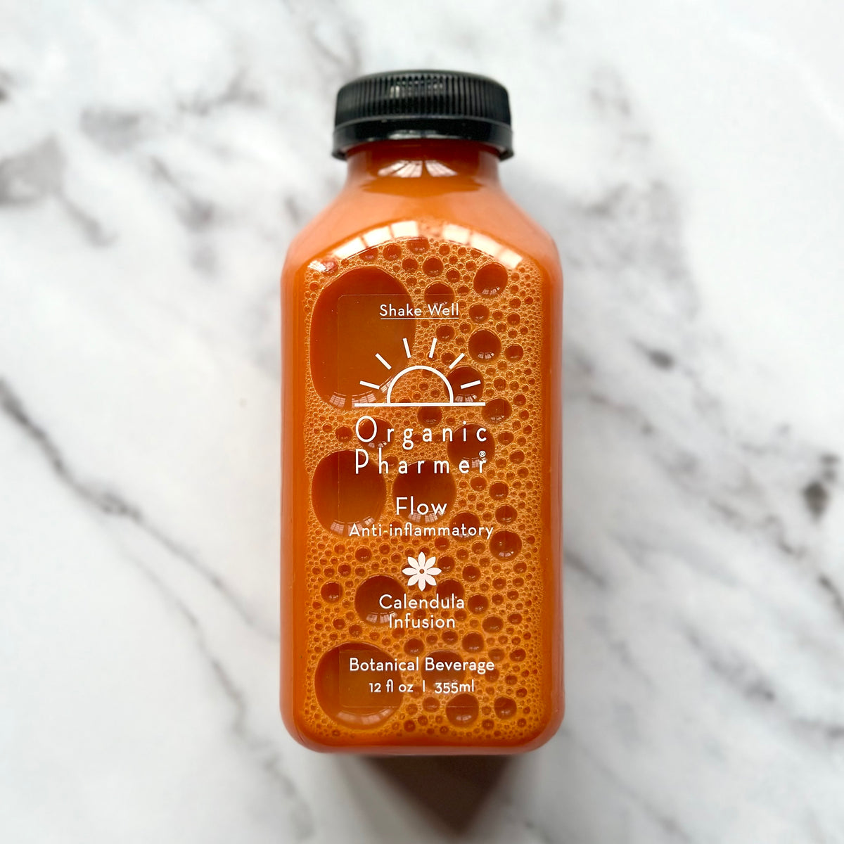 A bottle of Organic Pharmer Flow Botanical Beverage with a orange-hued liquid visible through the clear bottle. The label displays the brand name, product name, and the phrase 'Botanical Beverage.