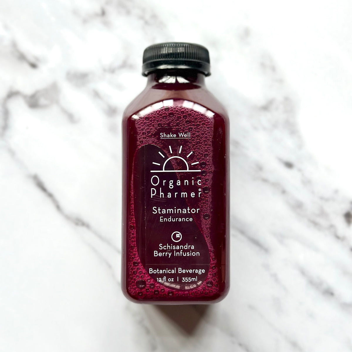 A bottle of Organic Pharmer Staminator, a botanical beverage with schisandra berry infusion, on a marble background.